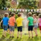 Kinder spielen bei einem Kindergeburtstag am Rasensprenger, Wasserbomben im Eimer